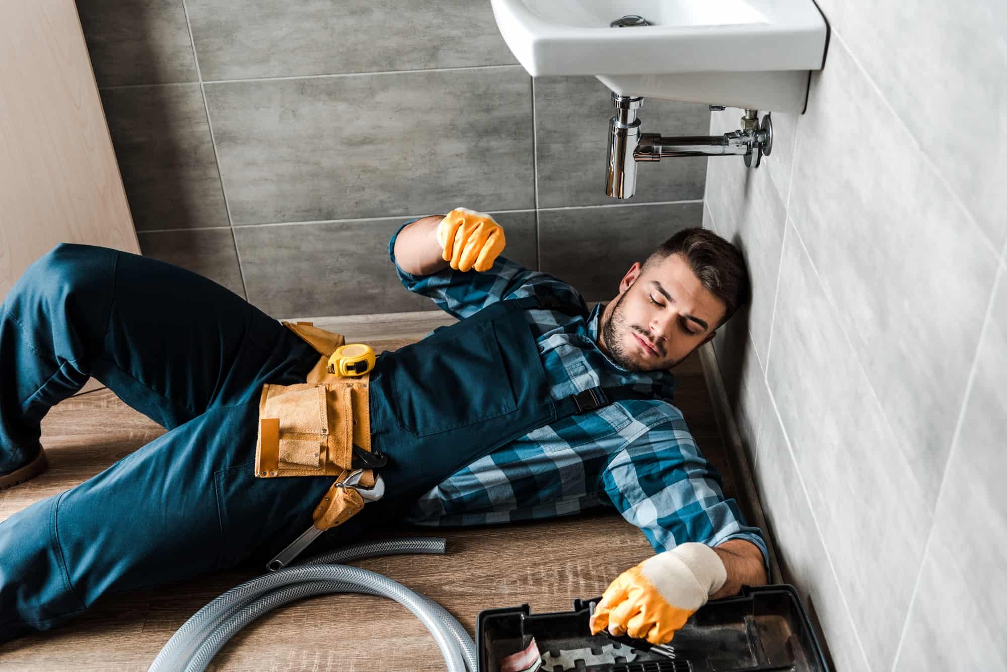 bearded-handyman-lying-on-floor-near-toolbox-in-bathroom.jpg